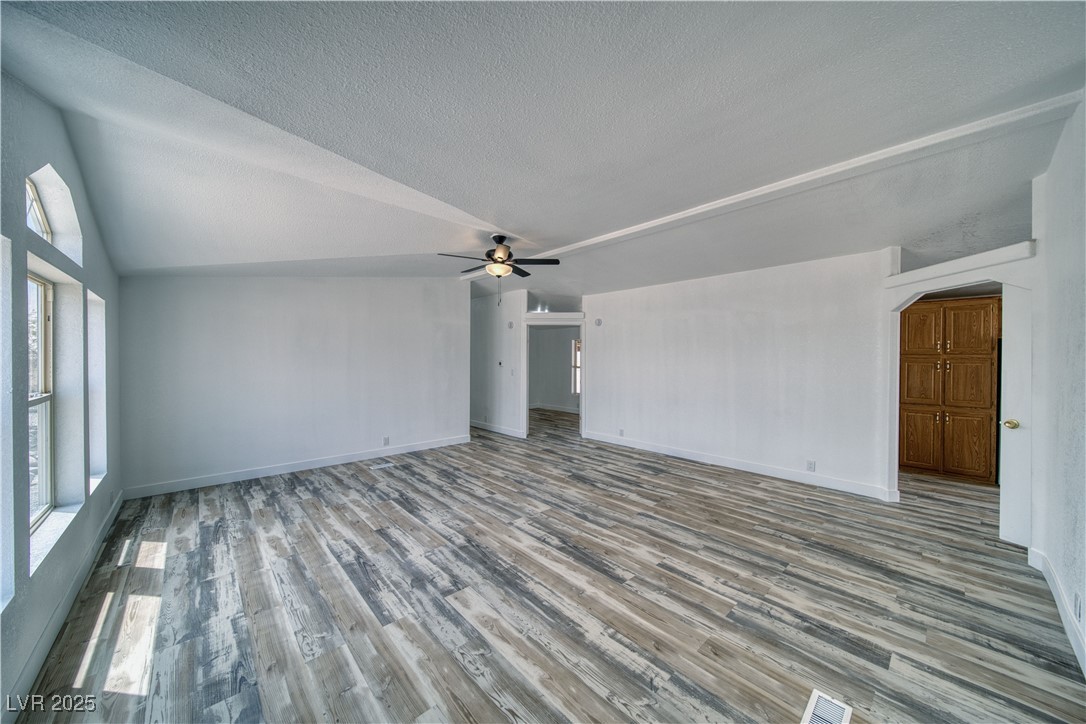 1340 South Adams Road Pahrump, NV 89048 - Photo 5 of 31 Unfurnished living room with wood finished floors, a ceiling fan, arched walkways, a textured ceiling, and vaulted ceiling