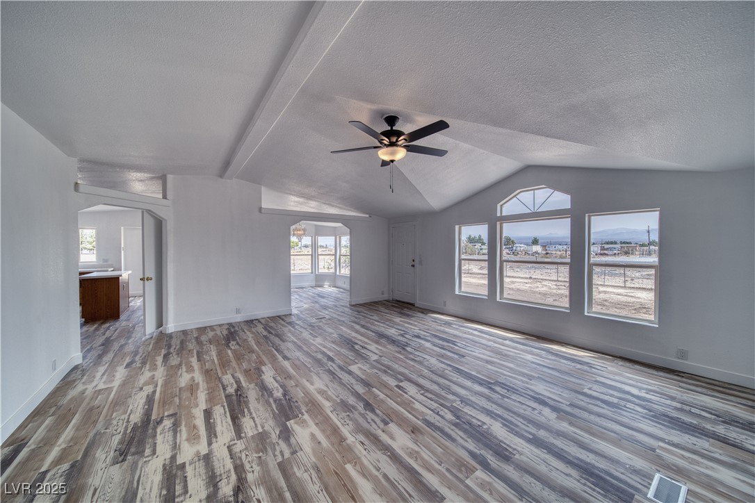 1340 South Adams Road Pahrump, NV 89048 - Photo 6 of 31 Unfurnished living room featuring vaulted ceiling, wood finished floors, arched walkways, a ceiling fan, and a textured ceiling