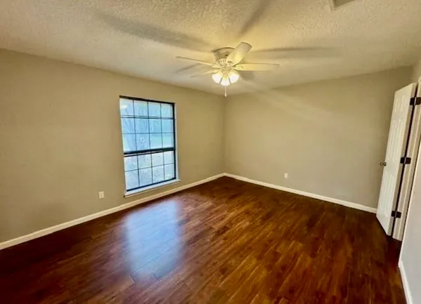 an empty room with wooden floor fan and windows