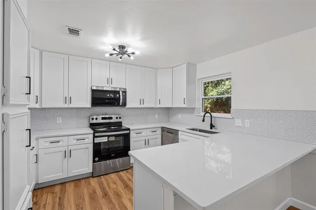 a kitchen with stainless steel appliances white cabinets a sink a stove a microwave and island