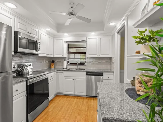 a kitchen with stainless steel appliances granite countertop a refrigerator a stove a sink dishwasher and white cabinets with wooden floor