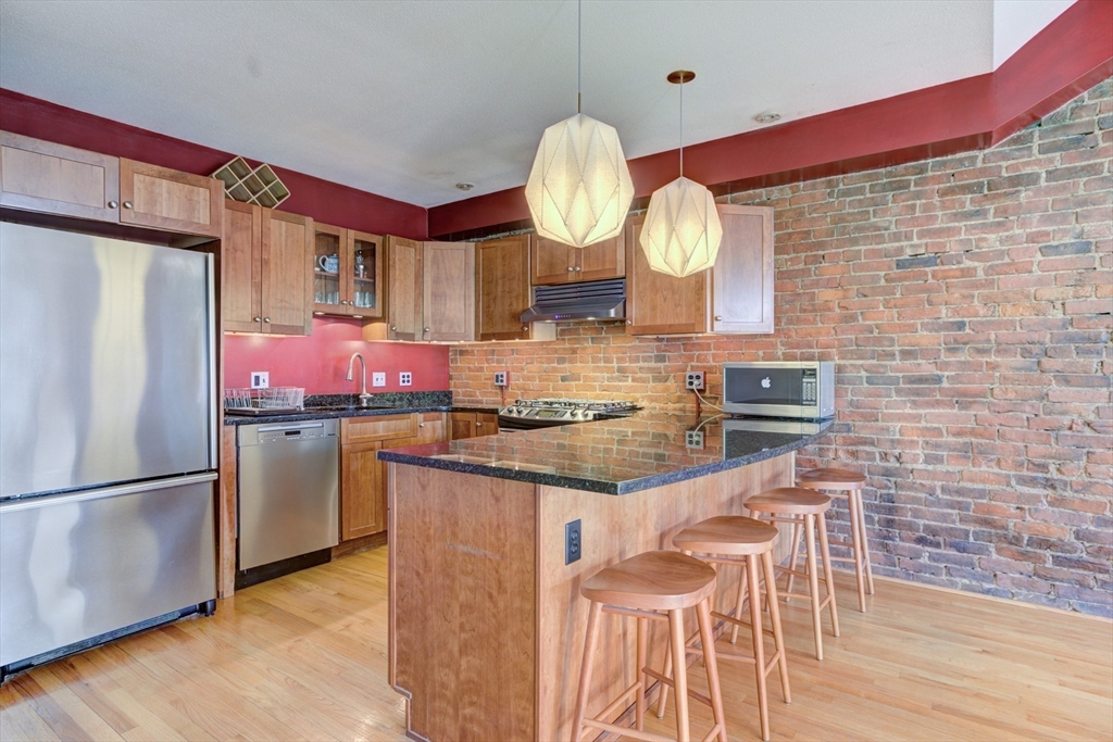 231 Main Street, Unit 3R Northampton, MA 01060 - Photo 8 of 23 a kitchen with stainless steel appliances granite countertop a sink refrigerator stove and wooden floor