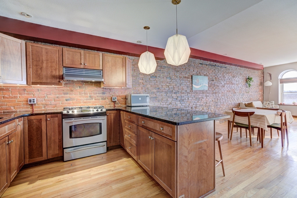 231 Main Street, Unit 3R Northampton, MA 01060 - Photo 9 of 23 a kitchen with stainless steel appliances granite countertop a stove a sink dishwasher and white cabinets with wooden floor