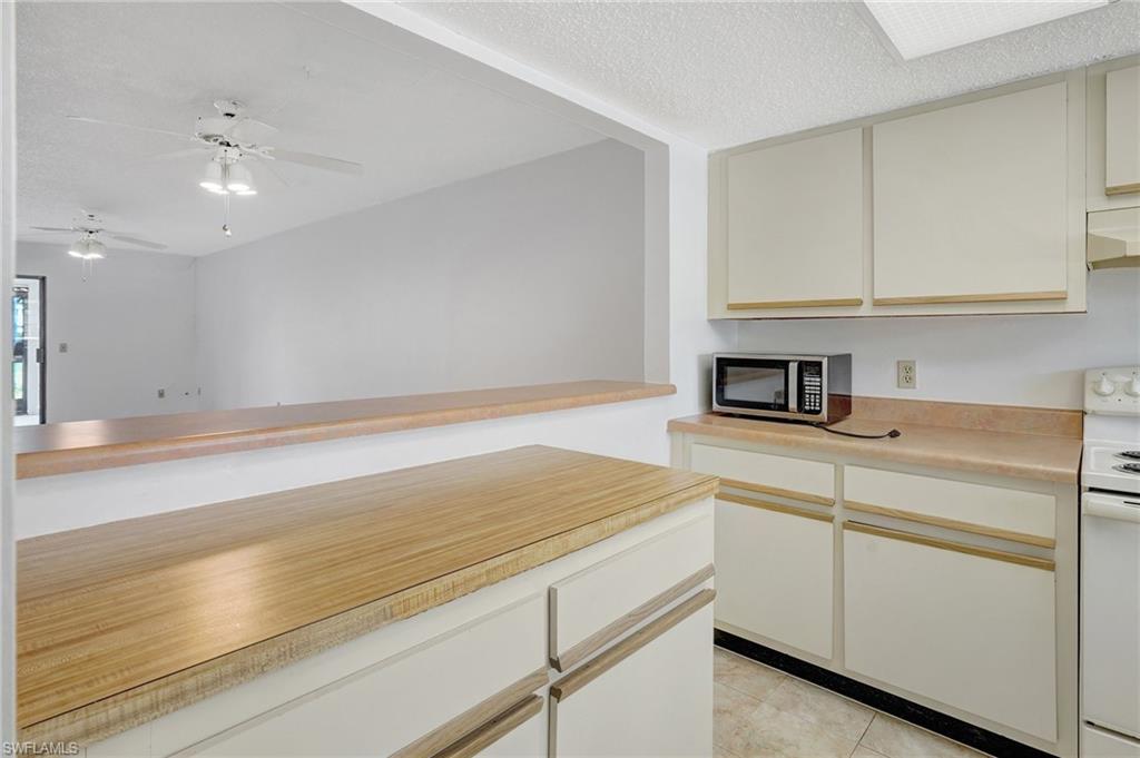 151 Cypress Way East, Unit D3 Naples, FL 34110 - Photo 5 of 46 Kitchen featuring white electric range oven, a textured ceiling, light countertops, stainless steel microwave, and light tile patterned floors