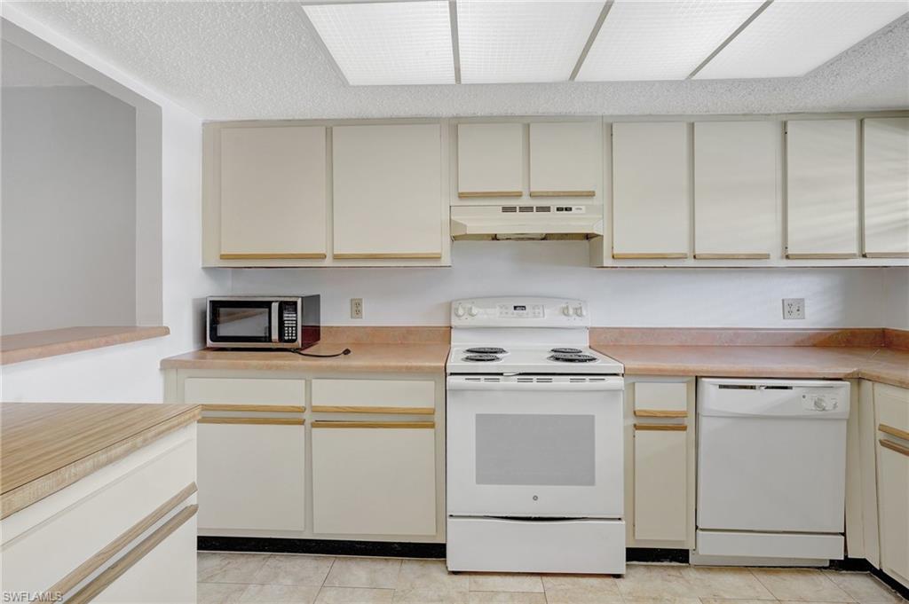 151 Cypress Way East, Unit D3 Naples, FL 34110 - Photo 6 of 46 Kitchen featuring white appliances, light countertops, cream cabinetry, and under cabinet range hood