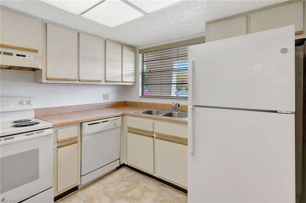 151 Cypress Way East, Unit D3 Naples, FL 34110 - Photo 7 of 46 Kitchen featuring light tile patterned flooring, cream cabinetry, white appliances, under cabinet range hood, and a sink
