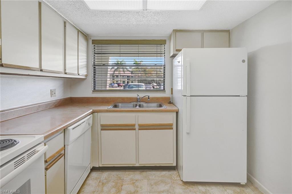 151 Cypress Way East, Unit D3 Naples, FL 34110 - Photo 9 of 46 Kitchen featuring light countertops, a sink, a textured ceiling, and white appliances