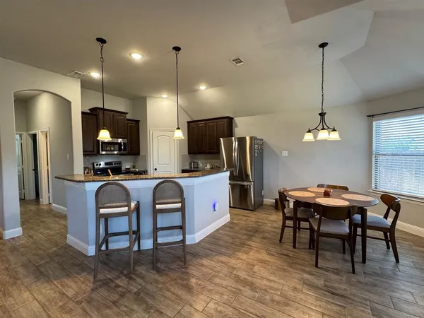 a kitchen with granite countertop kitchen island stainless steel appliances a dining table chairs sink and cabinets