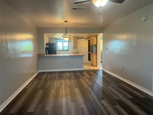 an empty room with wooden floor kitchen view and windows