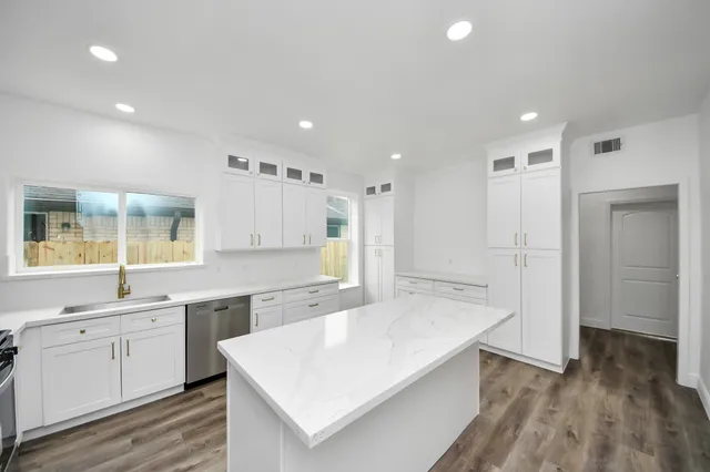 a large white kitchen with kitchen island a stove a sink a refrigerator and white cabinets with wooden floor