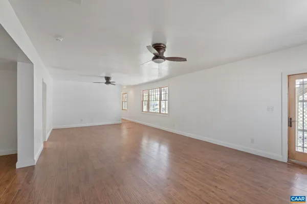 an empty room with wooden floor ceiling fan and windows