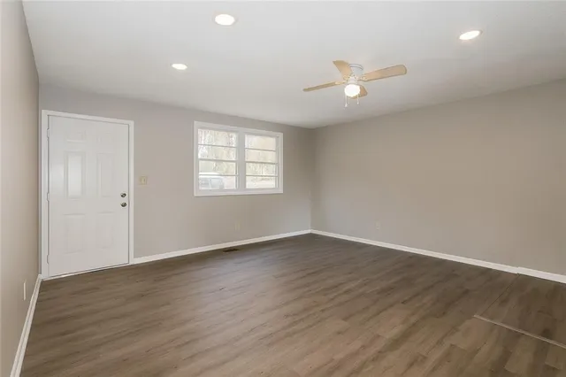 an empty room with wooden floor ceiling fan and windows