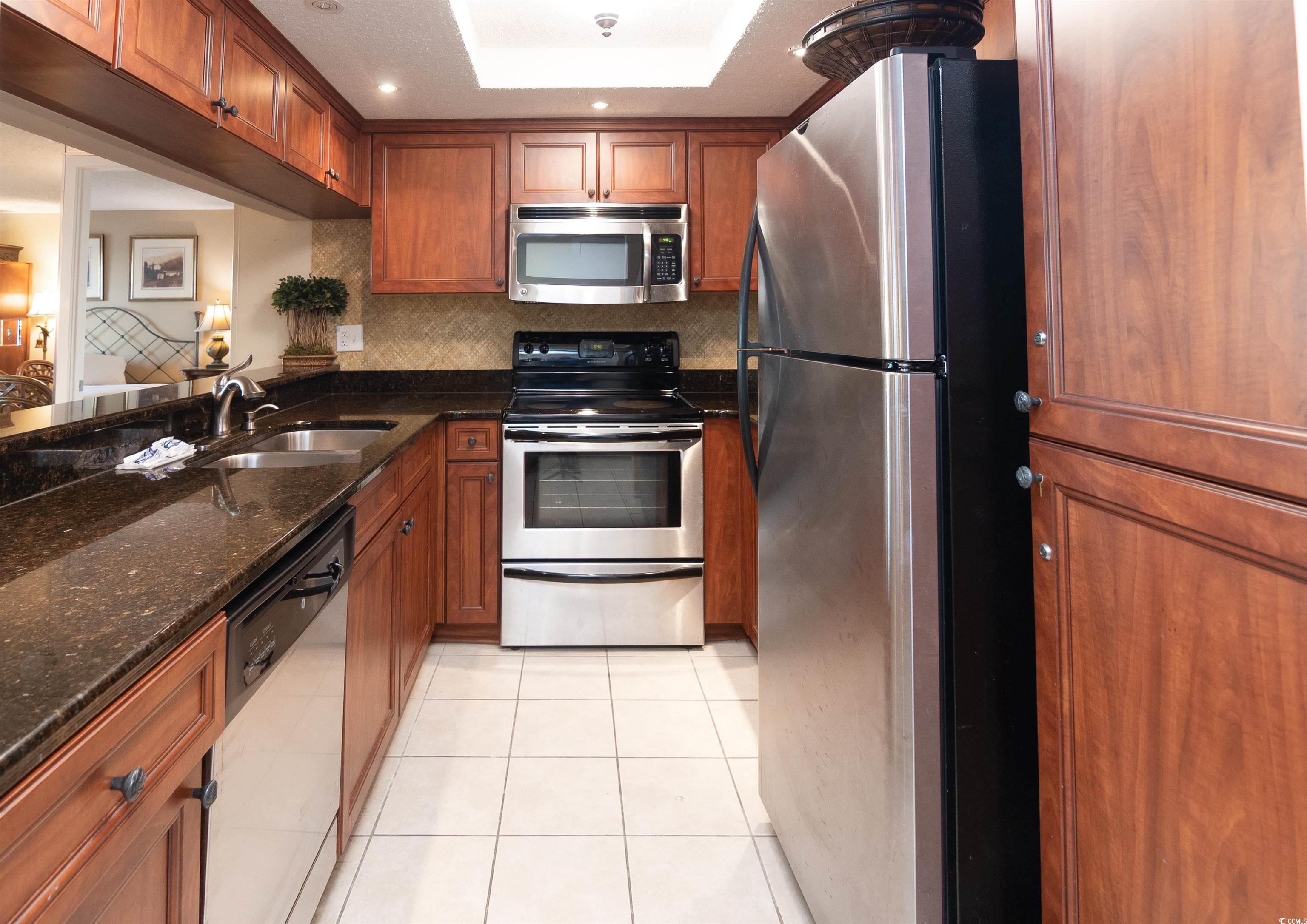 9820 Queensway Boulevard, Unit 1006 Myrtle Beach, SC 29572 - Photo 6 of 30 Kitchen with dark stone countertops, appliances with stainless steel finishes, brown cabinets, light tile patterned floors, and tasteful backsplash