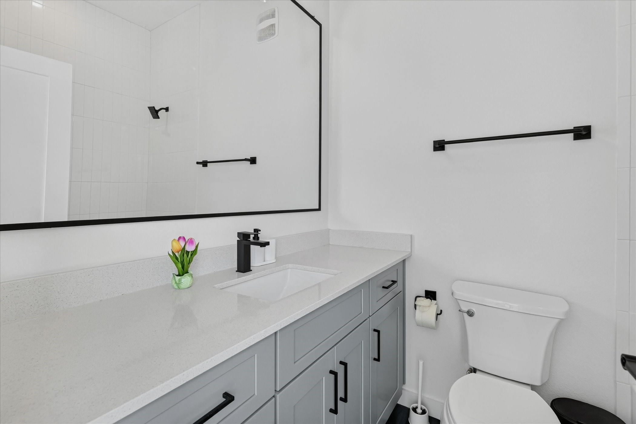 2000 Riverside Farms Road, Unit 8101 Austin, TX 78741 - Photo 33 of 41 This bathroom features a modern design with a sleek gray vanity, white countertop, and large mirror. It includes a toilet and a shower with a glass door. The space is well-lit and accented with black fixtures for a contemporary look.