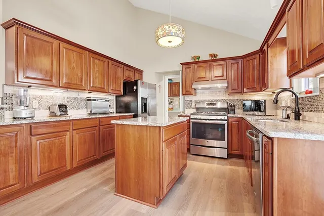 a kitchen with stainless steel appliances granite countertop a stove top oven a refrigerator a dining table and chairs with wooden floor