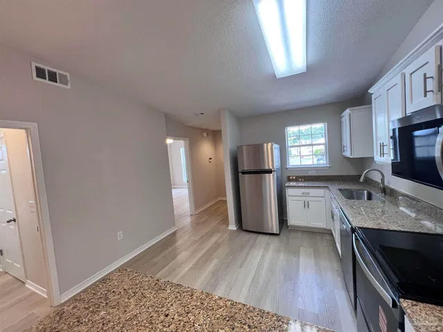 a kitchen with granite countertop a refrigerator a stove a sink cabinets and wooden floor