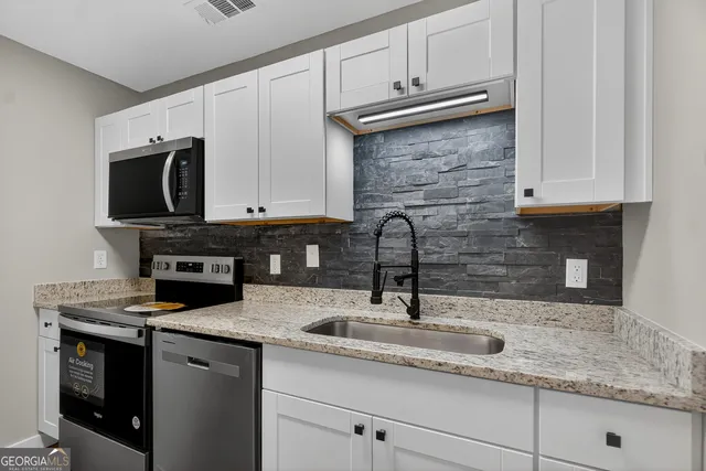 a kitchen with granite countertop a sink stainless steel appliances and white cabinets