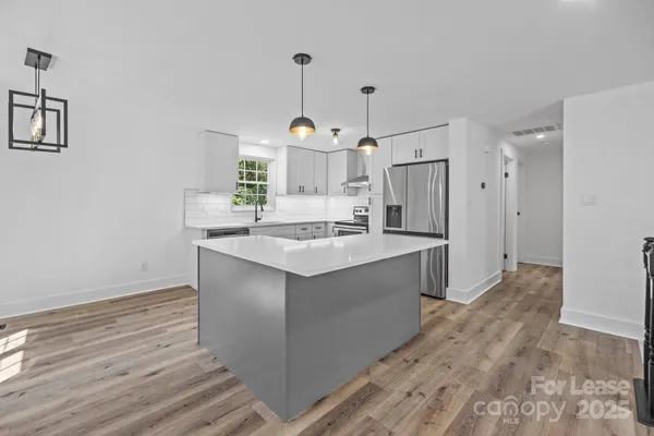 a kitchen with stainless steel appliances granite countertop a sink stove a refrigerator and white cabinets with wooden floor