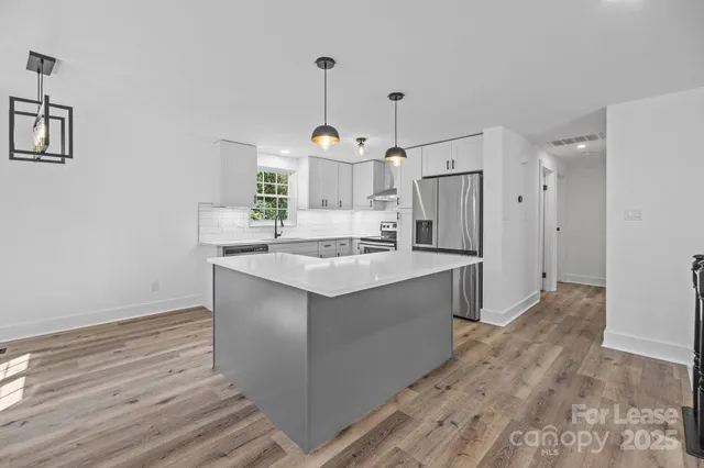 a kitchen with stainless steel appliances granite countertop a sink stove a refrigerator and white cabinets with wooden floor