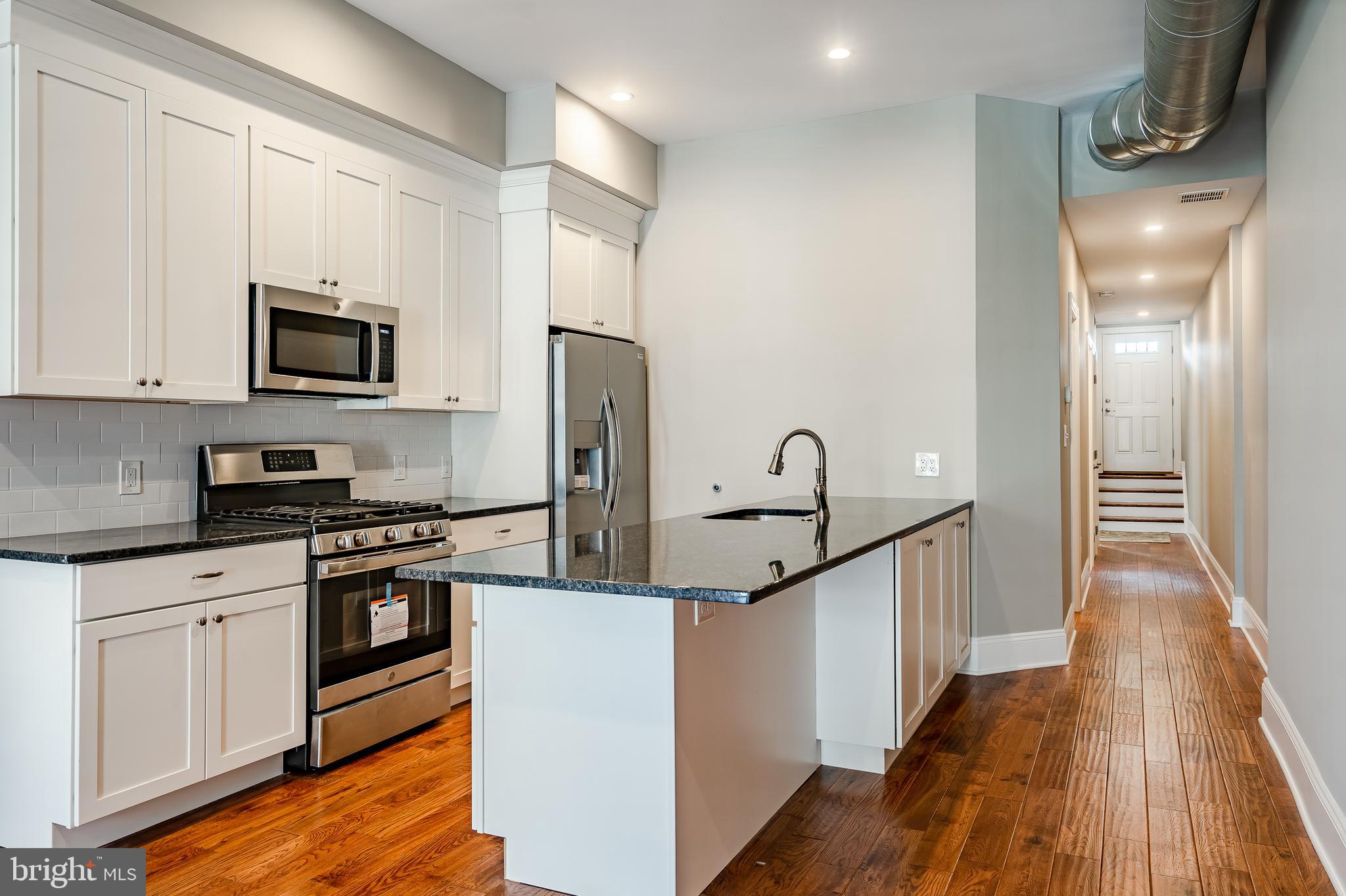 226 Bridge Street, Unit 2 Phoenixville, PA 19460 - Photo 8 of 25 a kitchen with granite countertop a refrigerator a stove top oven and wooden floor