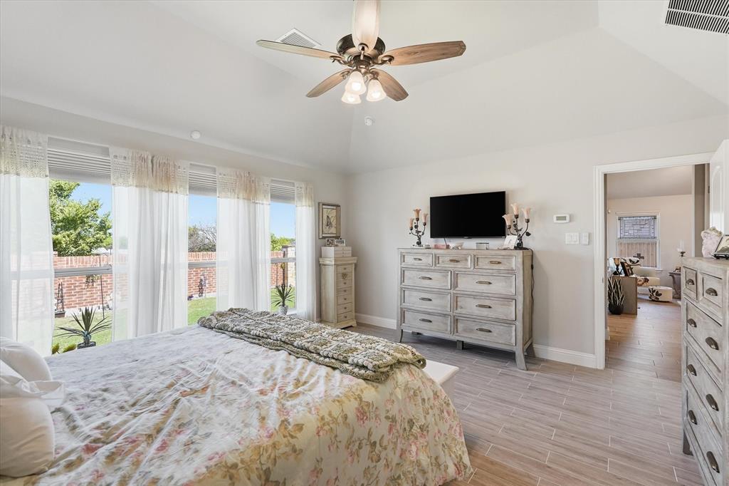 813 Mildren Lane Fate, TX 75087 - Photo 10 of 32 The primary bedroom also features a wall of windows, a vaulted ceiling with ceiling fan and light fixture and easy access to the main parts of the home.
