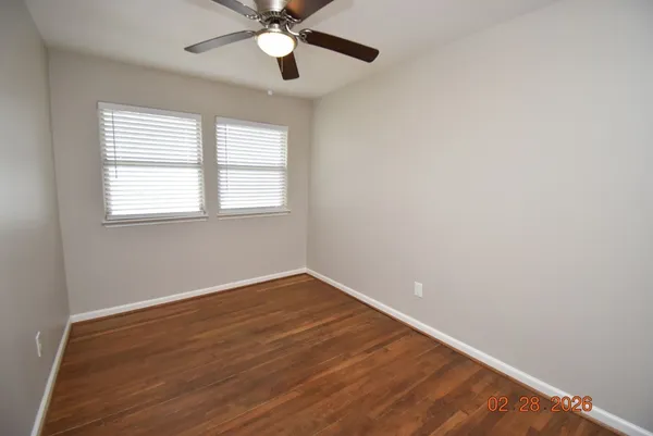 an empty room with wooden floor fan and windows