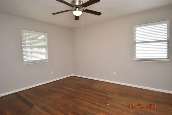 an empty room with wooden floor fan and windows