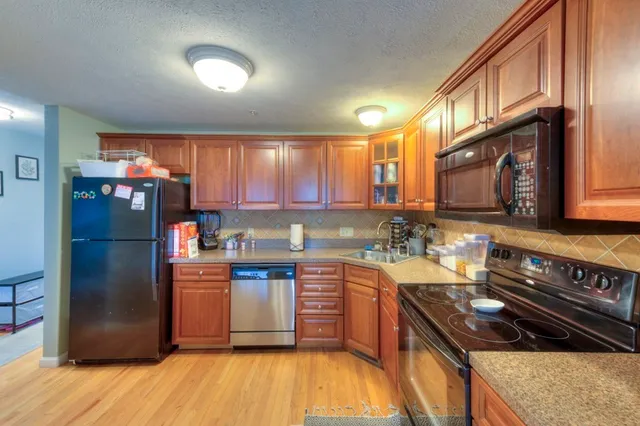 a kitchen with stainless steel appliances granite countertop a refrigerator a sink dishwasher a stove and a dining table with wooden floor