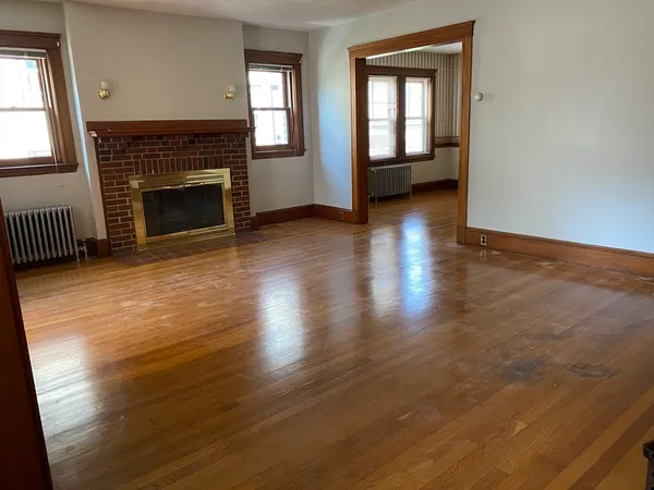an empty room with wooden floor fireplace and windows
