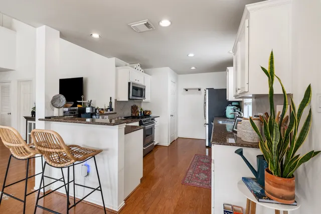 a kitchen with stainless steel appliances a refrigerator a sink a stove a dining table and chairs with wooden floor