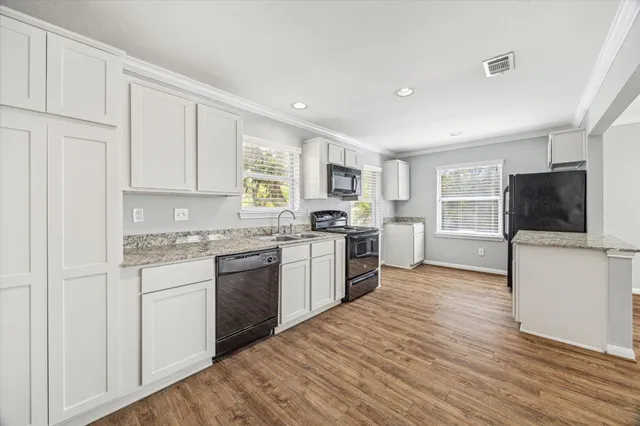 a kitchen with stainless steel appliances granite countertop a stove top oven a sink dishwasher and a refrigerator with wooden floor