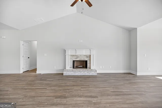 a view of an empty room with wooden floor fireplace and a window