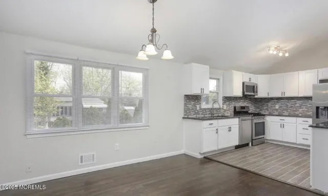 a large kitchen with granite countertop a stove and white cabinets with wooden floor