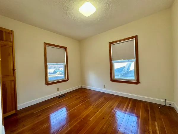 a view of an empty room with window and wooden floor