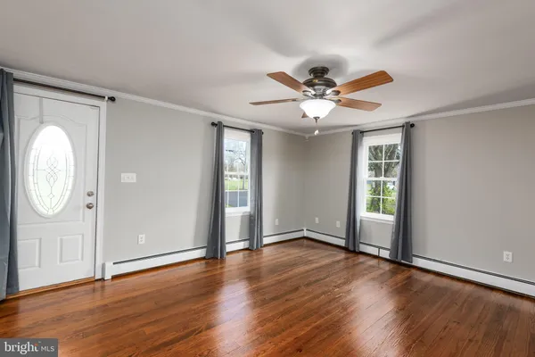 an empty room with wooden floor a ceiling fan and windows