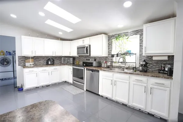 a kitchen with granite countertop white cabinets white appliances a sink and a window
