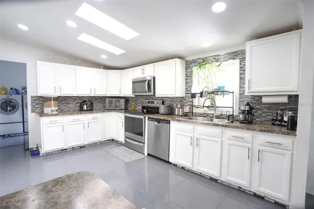 a kitchen with granite countertop white cabinets white appliances a sink and a window