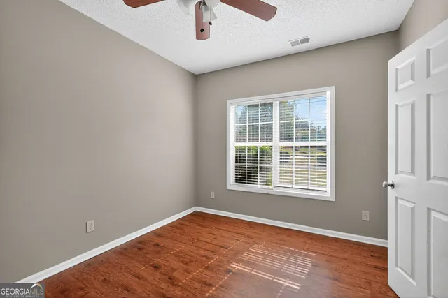 an empty room with wooden floor fan and windows