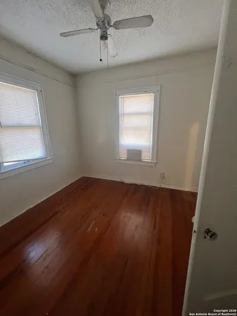 an empty room with wooden floor fan and windows