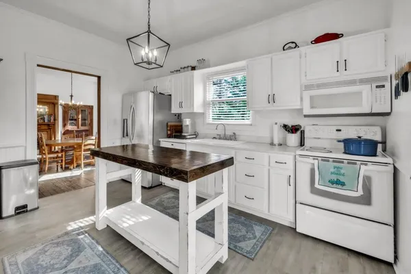 a kitchen with stainless steel appliances kitchen island granite countertop a refrigerator a sink a stove and white cabinets with wooden floor