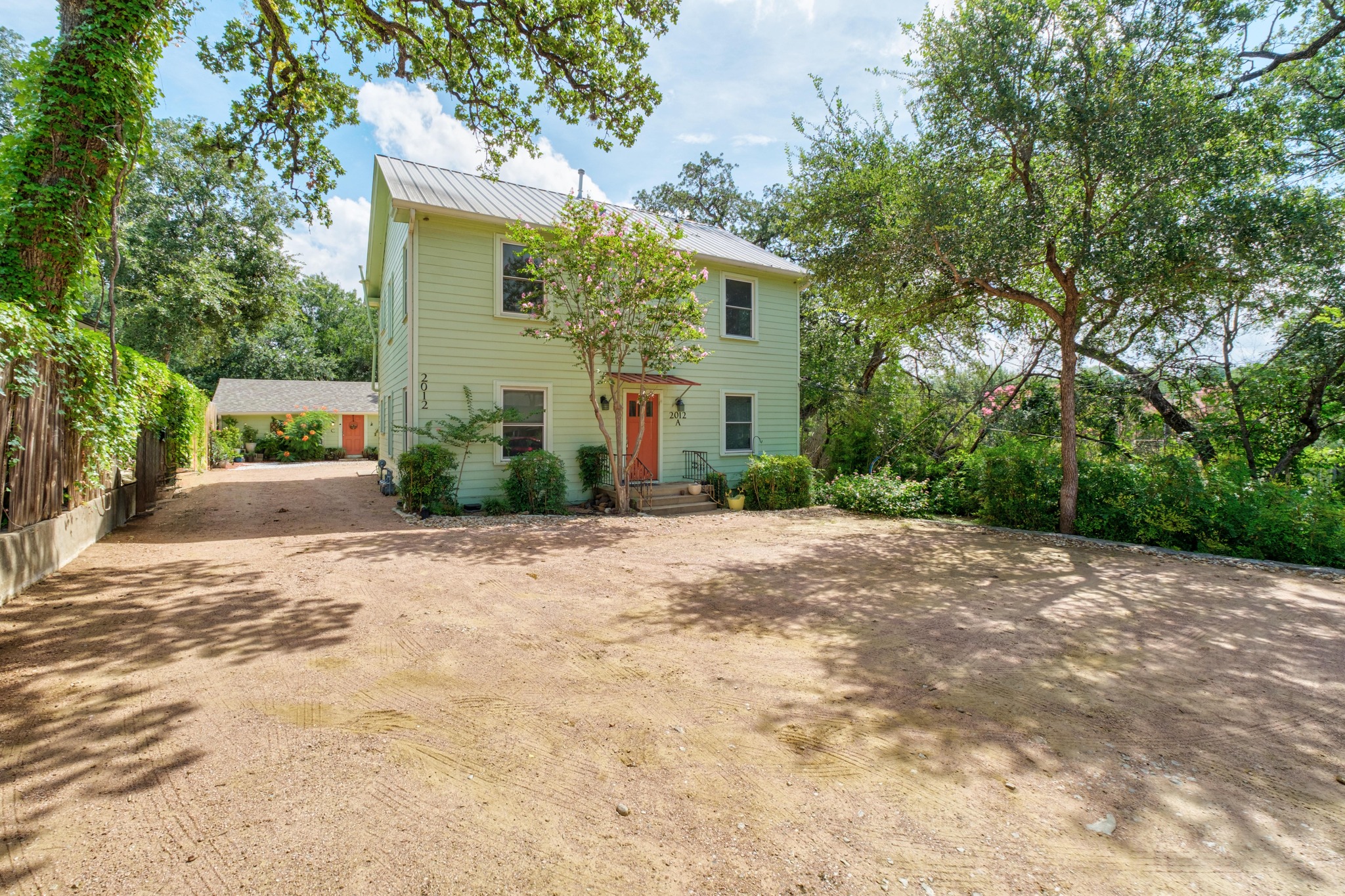 2012 Enfield Road, Unit B Austin, TX 78703 - Photo 1 of 20 A classic facade with a welcoming orange door, framed by mature trees and lush green foliage.