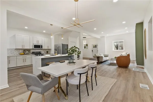 a kitchen with stainless steel appliances kitchen island granite countertop a dining table chairs refrigerator and microwave