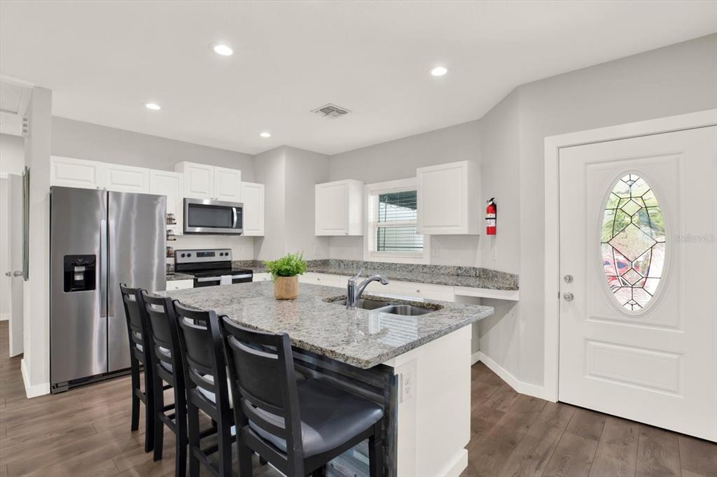 3023 Muir Street Holiday, FL 34691 - Photo 5 of 25 a kitchen with stainless steel appliances granite countertop a stove a refrigerator a microwave a sink and white cabinets with wooden floor