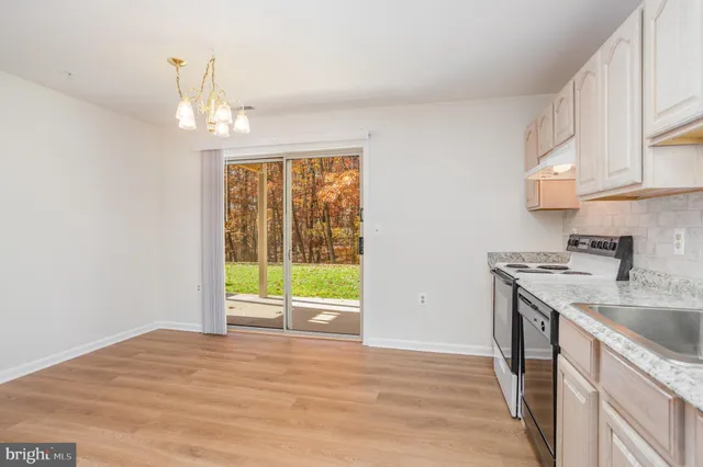 a kitchen with granite countertop a refrigerator oven a sink dishwasher and white cabinets with wooden floor