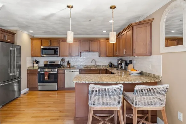 a kitchen with stainless steel appliances granite countertop a stove top oven a refrigerator a sink and chairs