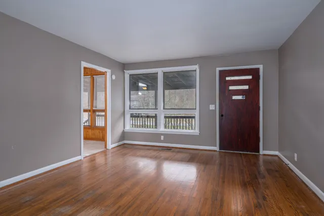 a view of an empty room with wooden floor and a window