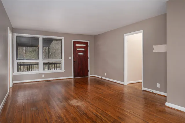 a view of an empty room with wooden floor and a window