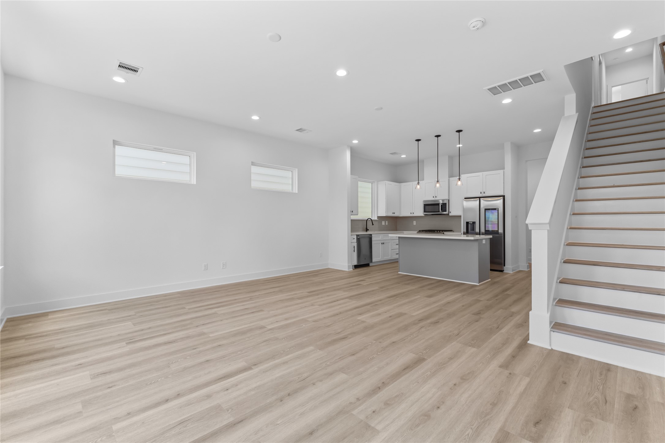 3426 Bolin Road Houston, TX 77092 - Photo 12 of 34 This is a modern, open-concept living space featuring light color floors, a fresh white kitchen with an island and pendant lighting, and a staircase leading to the upper level. Bright and airy with recessed lighting and a neutral color palette.