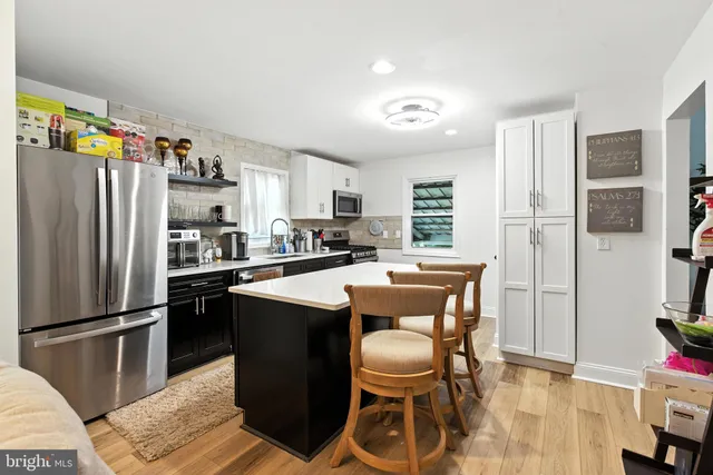 a kitchen with stainless steel appliances a refrigerator a stove a sink a dining table and chairs with wooden floor