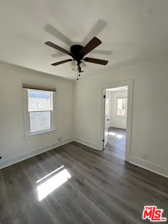 an empty room with wooden floor chandelier fan and windows